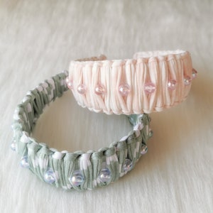 Puede incluir: Dos diademas de tela con cuentas de imitación de perlas. La diadema superior es rosa y blanca, la diadema inferior es verde y blanca.