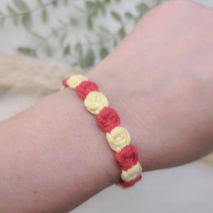 Op de afbeelding: Een rood en geel vriendschapsarmband met een geweven ontwerp.