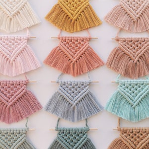 Peut inclure: Une collection de dix tentures murales en macramé de différentes couleurs, dont le rose, le bleu, le vert, le marron et le jaune. Chaque tenture présente un motif géométrique avec des détails en franges.