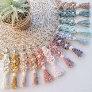 Op de afbeelding: Een verzameling van 12 handgemaakte macramé sleutelhangers met houten kralen en kwastjes in verschillende pastelkleuren, waaronder geel, roze, perzik, lavendel, blauw en groen.