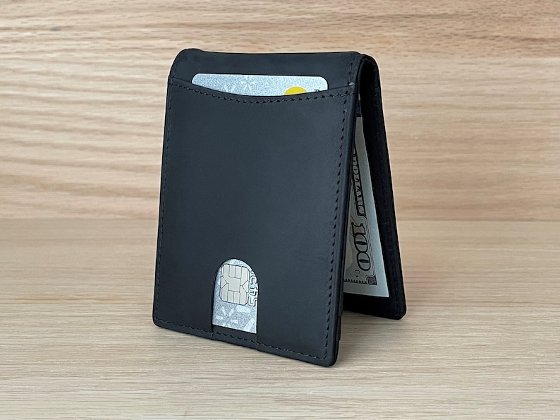 May include: A black leather wallet with a card slot and a cash pocket. The wallet is folded in half and has a bill sticking out of the cash pocket.