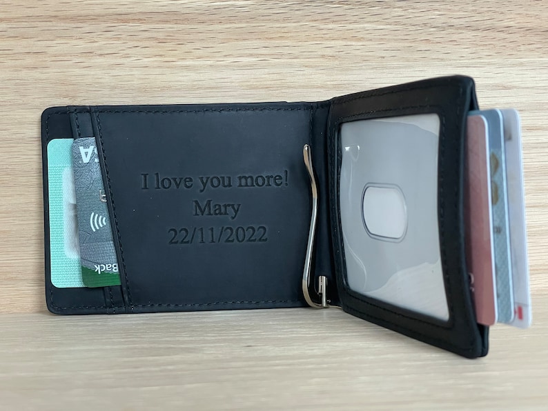 May include: Black leather wallet with a money clip and a clear ID window. The wallet has a personalized message that reads "I love you more! Mary 22/11/2022".