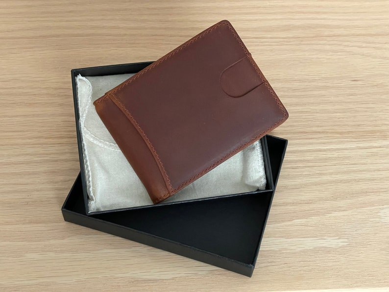 May include: A brown leather wallet in a black box with a white fabric lining. The wallet has a flap closure and a smooth leather finish.