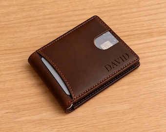 Peut inclure: Un portefeuille bifold en cuir marron foncé avec des coutures orange visibles, une fenêtre d'identification en plastique transparent et une fente pour carte. Le nom DAVID est gravé sur la surface avant. Le portefeuille a un profil fin.