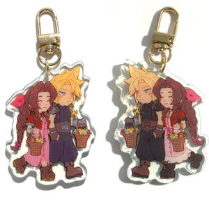 May include: Two acrylic keychains featuring a cartoon couple with blonde and brown hair, holding baskets. The keychains have gold-colored clasps. The characters are dressed in fantasy-style clothing, with one in a red outfit and the other in a dark blue outfit.
