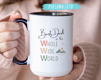 May include: White ceramic mug with a black interior and a navy blue handle. The mug features the text "Best Dad in the Whole Wide World" in a script font, with colorful lettering and a small mountain and sun graphic.