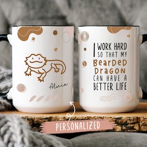 May include: White ceramic mug with a black handle. One side features a cartoon bearded dragon with the name "Alvin" printed below. The other side has the text "I work hard so that my Bearded Dragon can have a better life".