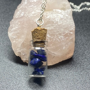 May include: A silver chain necklace with a small glass bottle pendant filled with blue lapis lazuli stones. The bottle has a cork stopper.