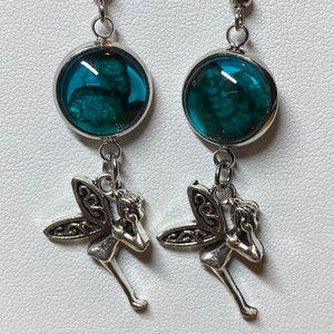 May include: Silver fairy dangle earrings with a teal blue glass cabochon. The cabochon has a swirling pattern.