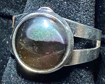Puede incluir: Un anillo de plata con una piedra grande, redonda e iridiscente engastada en el centro. El anillo tiene un diseño de doble banda.