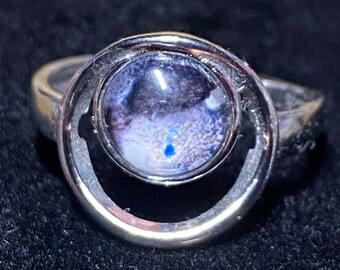 Puede incluir: Un anillo de plata con una piedra redonda, transparente, azul y blanca engastada en un círculo de plata.