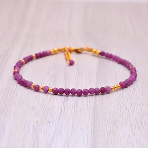 Könnte beinhalten: Ein zartes Armband aus rosafarbenen Edelsteinen mit goldenen Perlen. Das Armband besteht aus kleinen, runden Perlen und hat ein schlichtes, elegantes Design.