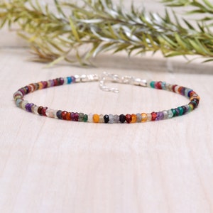 Puede incluir: Un delicado brazalete hecho con una variedad de cuentas de piedras preciosas de colores, incluyendo amatista, granate, citrino y esmeralda. El brazalete está enhebrado en una cadena de plata y tiene un cierre simple.