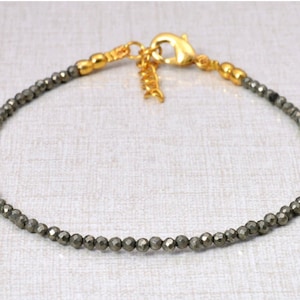 May include: A gold chain bracelet with small, dark gray beads. The bracelet has a lobster clasp.