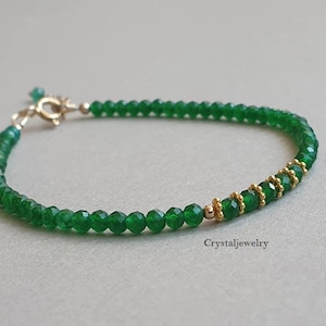 May include: A green gemstone bracelet with gold accents. The bracelet is made of small, faceted beads and has a silver clasp.