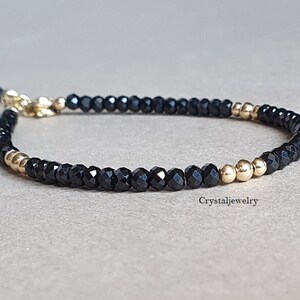 Puede incluir: Un brazalete de cuentas negras y doradas con cierre. El brazalete está hecho con pequeñas cuentas negras y tres cuentas doradas.