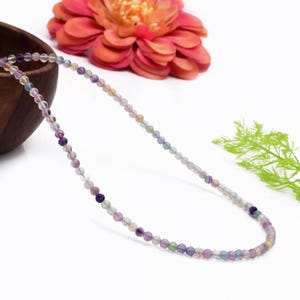 Puede incluir: Un collar de cuentas de fluorita multicolor con una variedad de tonos de morado, verde y rosa.