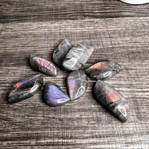 May include: A collection of seven iridescent labradorite stones in various shapes and sizes. The stones have a dark gray base with flashes of purple, blue, and green.