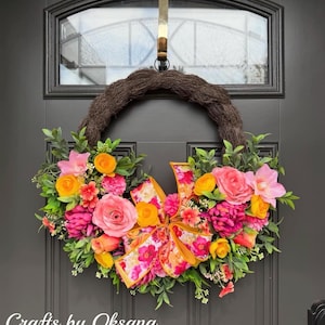 May include: A vibrant floral wreath with a brown base, adorned with pink, orange, and yellow flowers, and a patterned bow. The wreath hangs on a dark gray door. Text on the door reads "Crafts by Oksana."