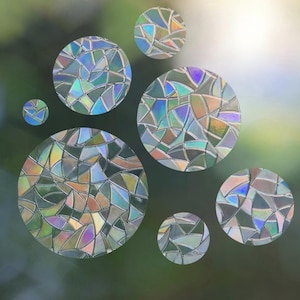 Könnte beinhalten: Sechs kreisförmige Fensteraufkleber mit einem Mosaikmuster aus irisierenden, mehrfarbigen Scherben. Die Aufkleber zeigen einen reflektierenden, prismatischen Effekt mit verschiedenen Blau-, Grün- und Orangetönen in einem Splitter-Design.