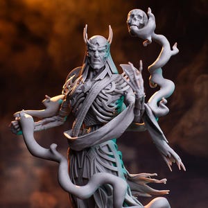 Op de afbeelding: Een gedetailleerd grijs beeldhouwwerk van een skeletfiguur met een kroon, die een staf met een schedel vasthoudt, en een figuur die eronder knielt. Het beeldhouwwerk heeft een donkere achtergrond en de tekst "PATREON HELL CREATOR".