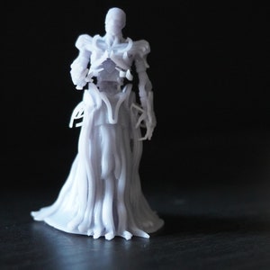 Puede incluir: Una figura blanca impresa en 3D de una figura esquelética que lleva una túnica fluida. La figura tiene una estructura esquelética detallada y una túnica larga y fluida que se drape alrededor de su cuerpo.