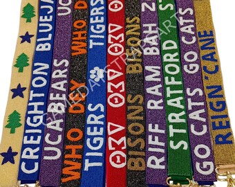 Könnte beinhalten: Eine Sammlung von 10 Perlenbändern mit verschiedenen College-Teamnamen und -logos. Die Bänder sind aus bunten Perlen gefertigt und haben goldene Verschlüsse. Die Bänder sind in einer Reihe angeordnet, wobei die Namen und Logos zum Betrachter zeigen. Die Namen auf den Bändern sind Creighton Bluejays, UCA Bears, Who Dey, Tigers, 037, Bisons, Riff Ram Bah Zoo, Stratford, Go Cats Go und Reign Cane.