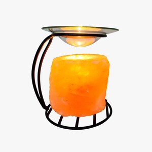 May include: A Himalayan salt lamp with a black metal stand and a glass dish on top. The salt lamp is lit and glowing orange.