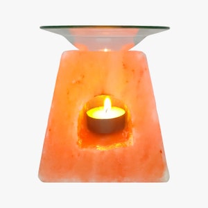 Puede incluir: Una lámpara de sal del Himalaya de color rosa con un plato de vidrio en la parte superior y una vela pequeña en el centro. La vela está encendida y la lámpara de sal brilla.