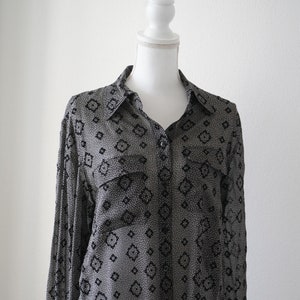 May include: A long-sleeved, button-down shirt with a black and white geometric pattern. The shirt is made of a sheer fabric and has a relaxed fit.