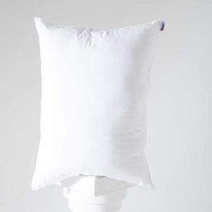 May include: A white pillow with a white fabric cover. The pillow is sitting on a white pedestal.