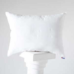 May include: A white pillow resting on a white pedestal. The pillow is made of a soft, smooth fabric.