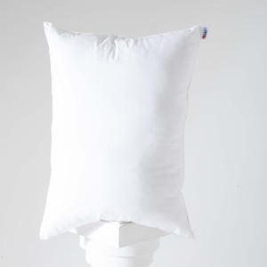 May include: A white pillow with a white fabric cover. The pillow is sitting on a white pedestal.