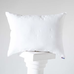 Puede incluir: Una almohada blanca descansando sobre un pedestal blanco. La almohada está hecha de una tela suave y lisa.