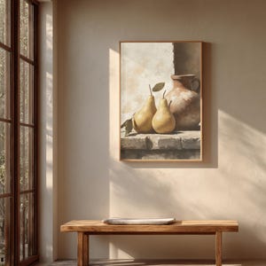 May include: A framed wall art print featuring a still life painting of two yellow pears and a brown ceramic pitcher resting on a stone ledge. The composition uses neutral tones and soft lighting to depict the fruit and vessel against a textured wall.
