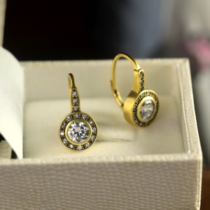 May include: A pair of gold hoop earrings with a single round clear stone set in a halo of smaller stones.