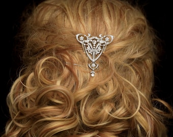 May include: A silver hair comb with a delicate, intricate design featuring clear rhinestones. The comb is in the shape of a teardrop and has a dangling rhinestone at the bottom.