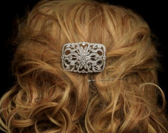 May include: A silver hair comb with a decorative design featuring a large, clear crystal in the center surrounded by smaller crystals.
