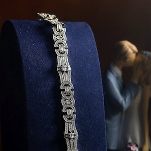 Può includere: Un braccialetto d'argento con un design geometrico decorato con pietre di zircone cubico trasparenti. Il braccialetto è esposto su un supporto in velluto blu.