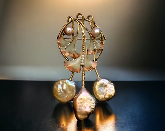 May include: A gold-tone brooch with a delicate design of stylized leaves and pearls. The leaves are enameled in shades of pink and white, and the pearls are iridescent.