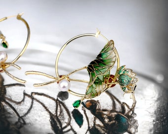 Op de afbeelding: Een paar gouden creolen met groene en witte emaille lotusbloemontwerpen. De oorbellen hebben parel- en groene edelsteenaccenten.