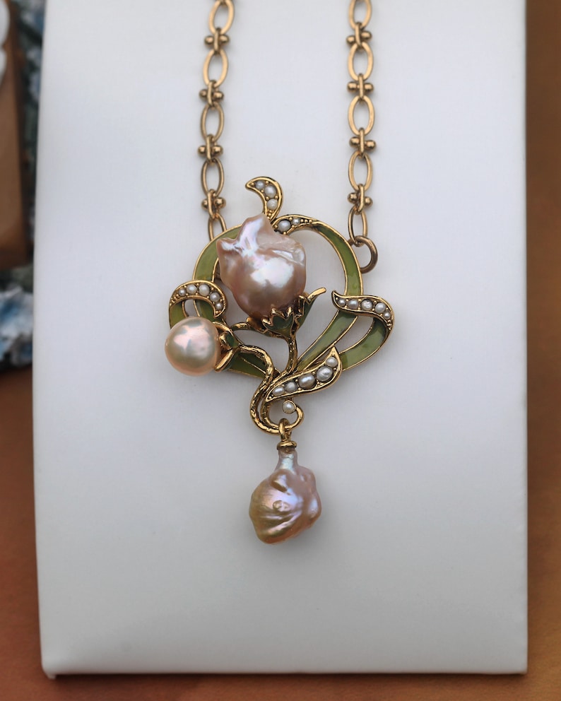May include: A gold necklace with a pendant featuring a pearl flower with green enamel accents and a dangling pearl drop.