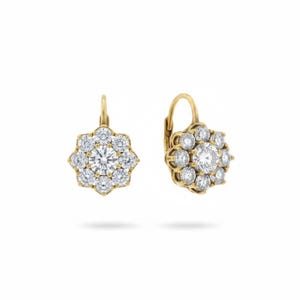 May include: A pair of gold-coloured leverback earrings. Each earring features a central, round, clear gemstone surrounded by smaller, clear gemstones, creating a floral or starburst design. The earrings are set against a white background.