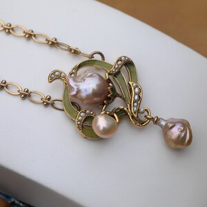 May include: A gold necklace with a green enamel pendant featuring a baroque pearl and smaller pearls. The pendant is shaped like a flower with a drop pearl hanging from the bottom.