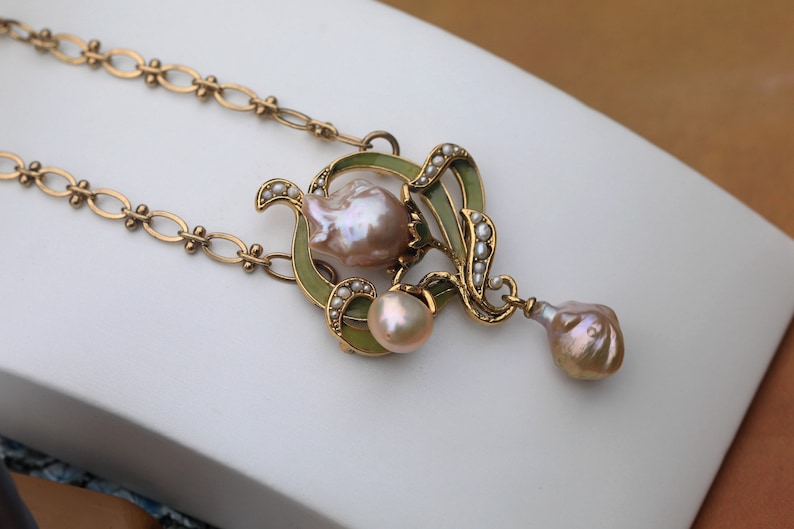 May include: A gold necklace with a green enamel pendant featuring a baroque pearl and smaller pearls. The pendant is shaped like a flower with a drop pearl hanging from the bottom.
