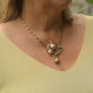May include: A gold chain necklace with a large, ornate pendant featuring a pearl and green enamel accents.