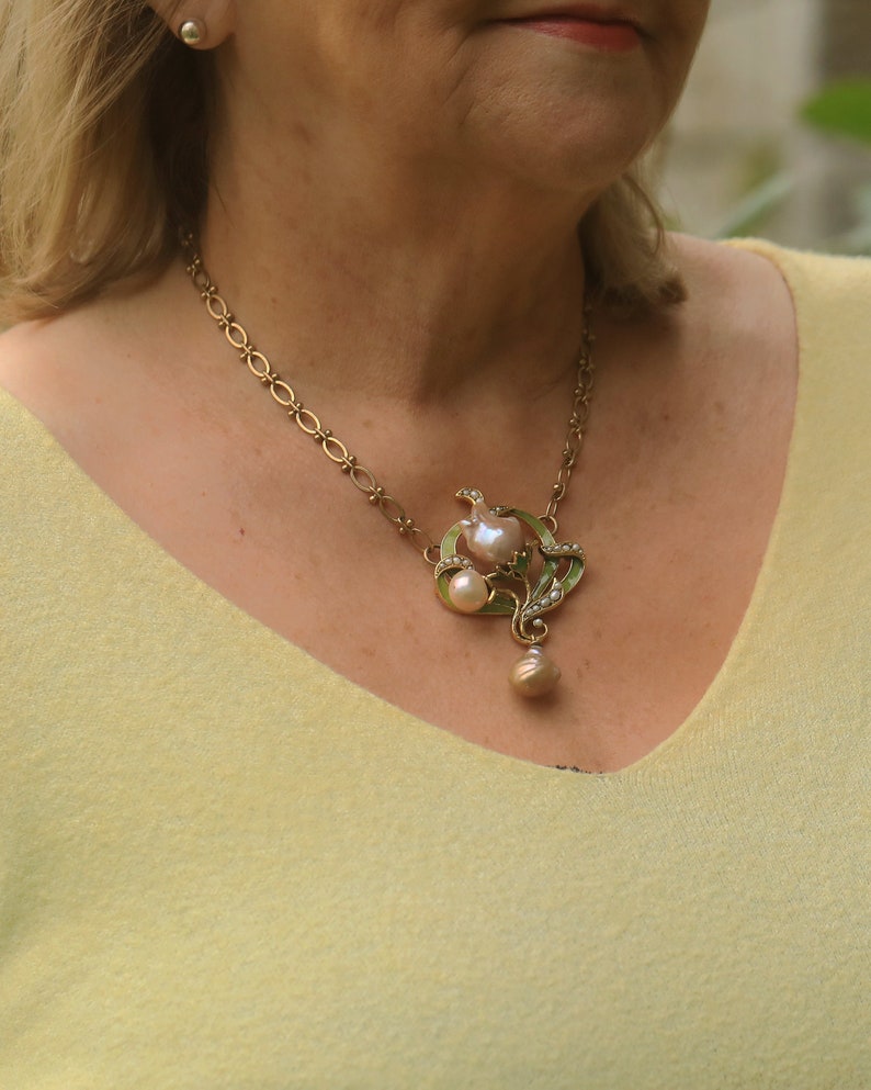 May include: A gold chain necklace with a large, ornate pendant featuring a pearl and green enamel accents.