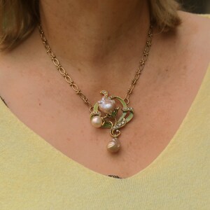 May include: A gold chain necklace with a pendant featuring a pearl flower with green enamel leaves and a pearl drop.