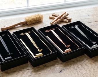Könnte beinhalten: Vier Sicherheitsrasierer in einzelnen schwarzen Geschenkboxen, in einer Reihe angeordnet. Die Rasierer sind in den Ausführungen Mattschwarz, poliertes Gold, Roségold und Chrom erhältlich. Jedes Set enthält einen passenden Griff und einen separaten Rasierkopf.