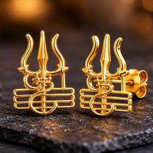 May include: A pair of gold-colored stud earrings. Each earring features a trident design with intricate detailing. The earrings are displayed on a dark, textured surface, showcasing their bright, reflective finish.